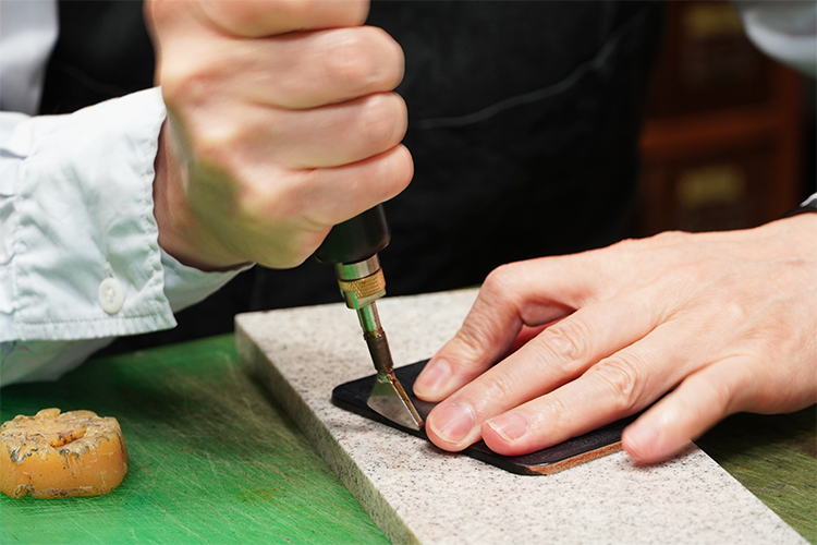 The process of polishing the edge of the leather. After smoothing it with a file, it is dyed, coated with funori seaweed and polished. Finally, beeswax is poured in and heated with a special tool to achieve a smooth finish.