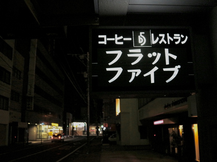 Beyond the sign, the lights of the arcade street shine