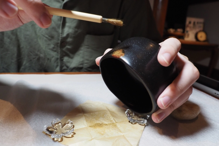 A Kintsugi experience where gold powder is sprinkled on a vessel to decorate it