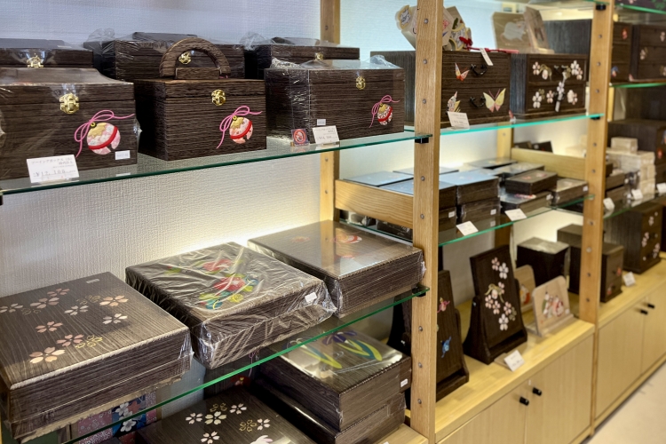Paulownia wood products such as sewing boxes and writing boxes are displayed in stores. Popular designs include bells, butterflies, and cherry blossoms.