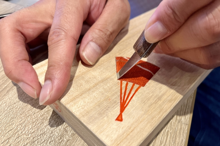 In "Kiri-mokumekomi" (paulownia wood inlay) crafts, the edge of the cloth is pressed into the grooves carved with a carving knife using a spatula.